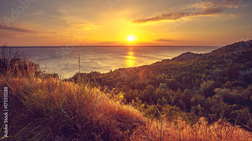 Majestic nature landscape with sunset bright sky, river and forest. Exploring beauty world: Ukraine, Europe. Travel, hiking, holidays, recreation. Travel background. Autumn season. Orange toning