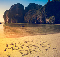 Happy Mother's Day written on the sand on a flat yellow beach. Mountains and clear ocean in the background. Phi-Phi Island, Thailand. Holiday, travel, sport, recreation. Retro vintage toning effect