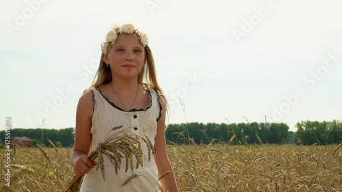 Close up of a girls hand playing in a grassy field, the golden field. The girl with a wreath on the head rejoices and pragat with wheat ears in hands outdoors. The young lovely girl jumps across the photo