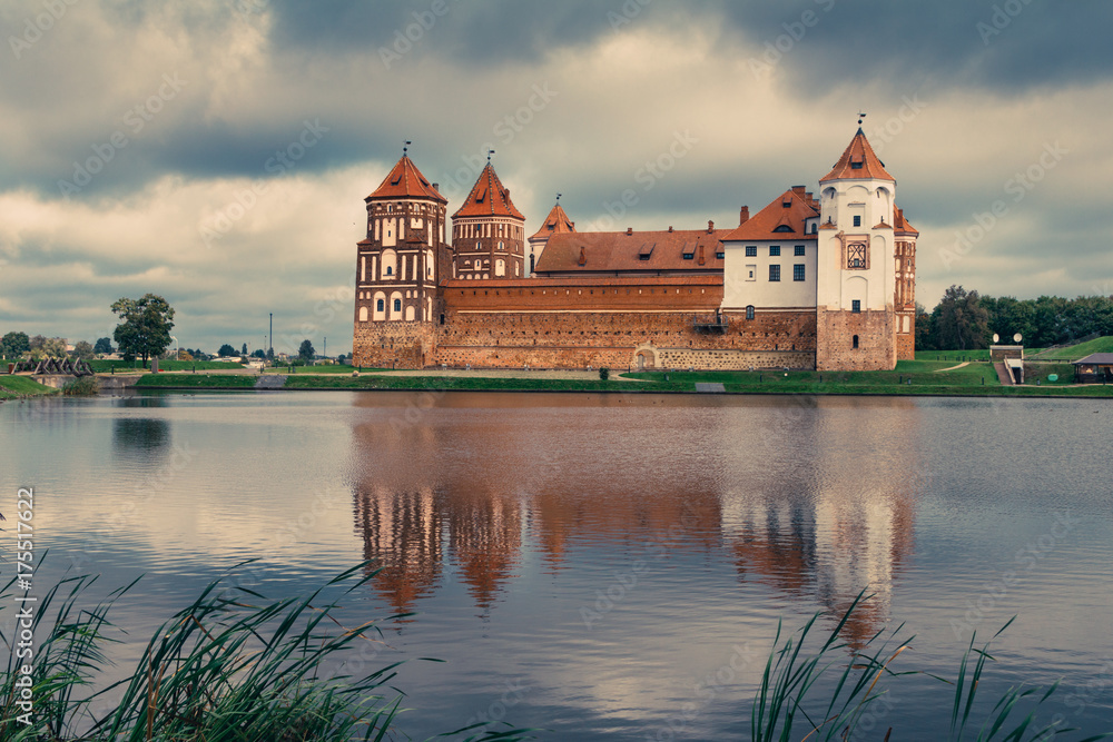 View of Mir Castle - ancient medieval fortress on the shore of the lake, reflecting in the water. Dramatic cloudy sky. Architectural monument of the Belarus. UNESCO World Heritage. Vintage effect. 