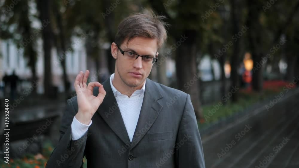 Businessman hand showing OK sign, autumn street background. Slow motion. Portrait of young successful confident businessman in the city. Man in a business suit. Businessman hand showing OK sign, autumn street background. Slow motion. Portrait of young successful confident businessman in the city. Man in a business suit.