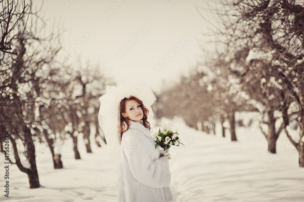 Beautiful ginger bride in a white fur coat with a bouquet of white flowers in a park. Winter wedding outdoors. Beautiful ginger bride in a white fur coat with a bouquet of white flowers in a park. Winter wedding outdoors.