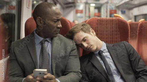  Tired businessman falling asleep on another passenger on commuter train