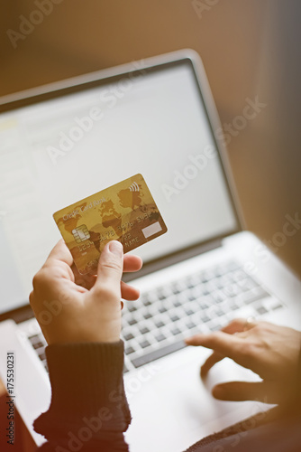 Crop shot from above of woman holding credit card while purchasing online with laptop.