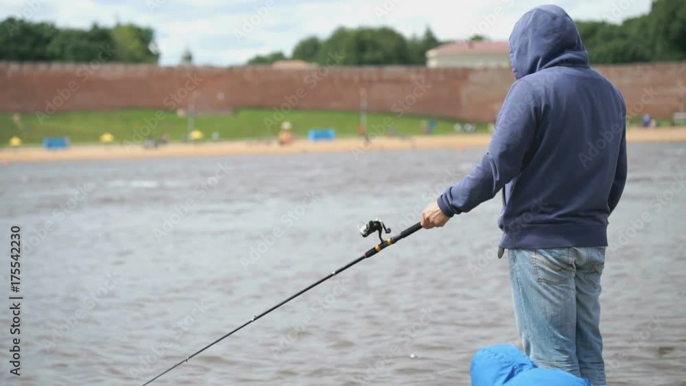 Father and son dressed in casual clothes is fishing with fishing rod on the background of river in a overcast summer day Father and son dressed in casual clothes is fishing with fishing rod on the background of river in a overcast summer day