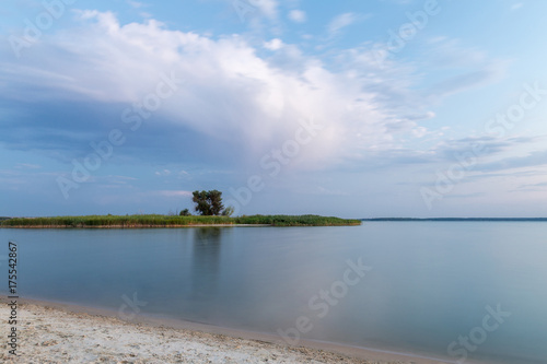 Beautiful scenic landscape of river or lake bank  calm water and island with tree against dramatic cloudy sky
