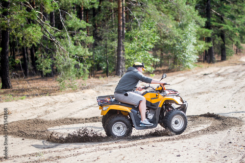 An ATV quadbike driver drifts and stunts on a sand rough terrain near forest