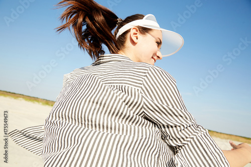 A girl walking in a black and white stripes shirt and a visor hat around a beach enjoying the sun photo