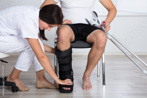 Female Doctor Putting Walking Brace On Person's Leg