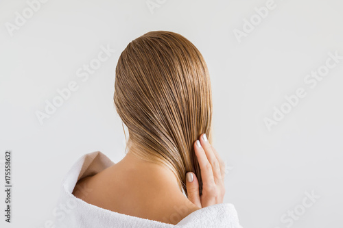 Woman in the white towel touching her wet blonde hair after shower on the gray background. Cares about a healthy and clean hair. Beauty salon concept.
