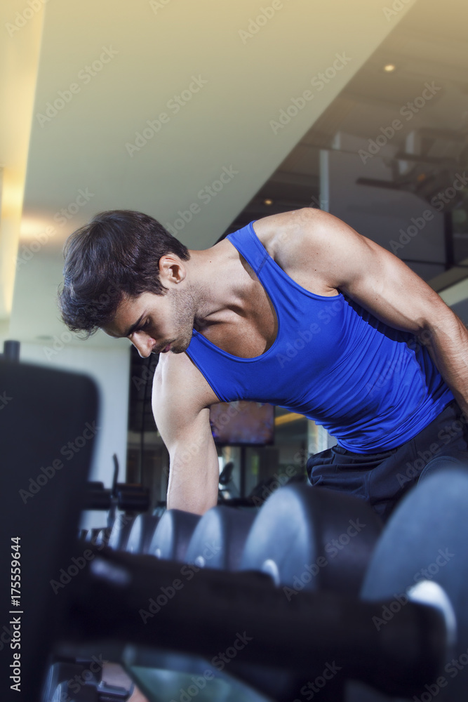 Young handsome muscular man exercising in the gym. Picking dumbbell from weight rack.