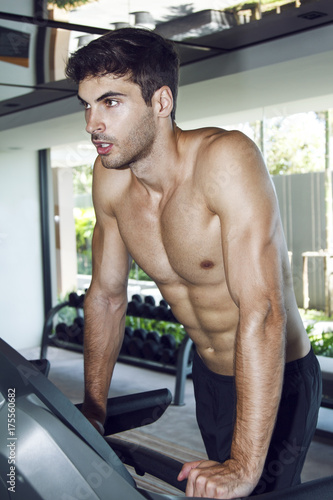 Young healthy handsome man training in the gym on the treadmill. Running with smile and without t-shirt. 
 photo