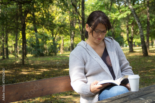 A middle-aged woman sitting on the bench in the park and reading a book