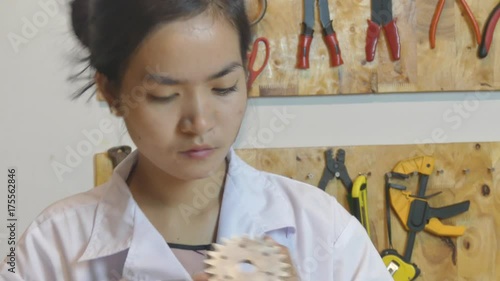 Medium close up of Asian  female youth as she measures the thickness of a machine gear in a maker lab.  She then makes notes and continues. photo