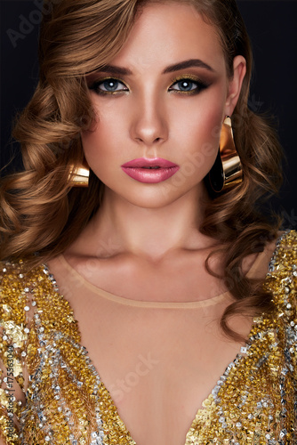 Glamour style beauty portrait. Fashion model in gold dress with perfect make up. Isolated on a black background.