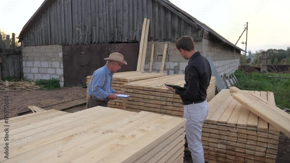 Worker And Businessman At Sawmill, Check Count Visiting Packed By Wooden Boards. Worker And Businessman At Sawmill, Check Count Visiting Packed By Wooden Boards.