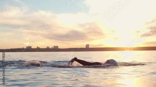 Tracking of triathlon sportswoman swimming with freestyle stroke in blue lake at sunset photo