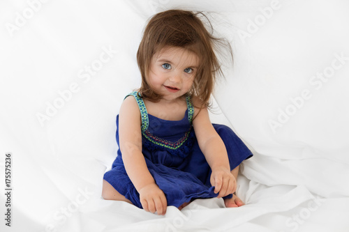 baby girl hiding under the sheets on a white bed photo