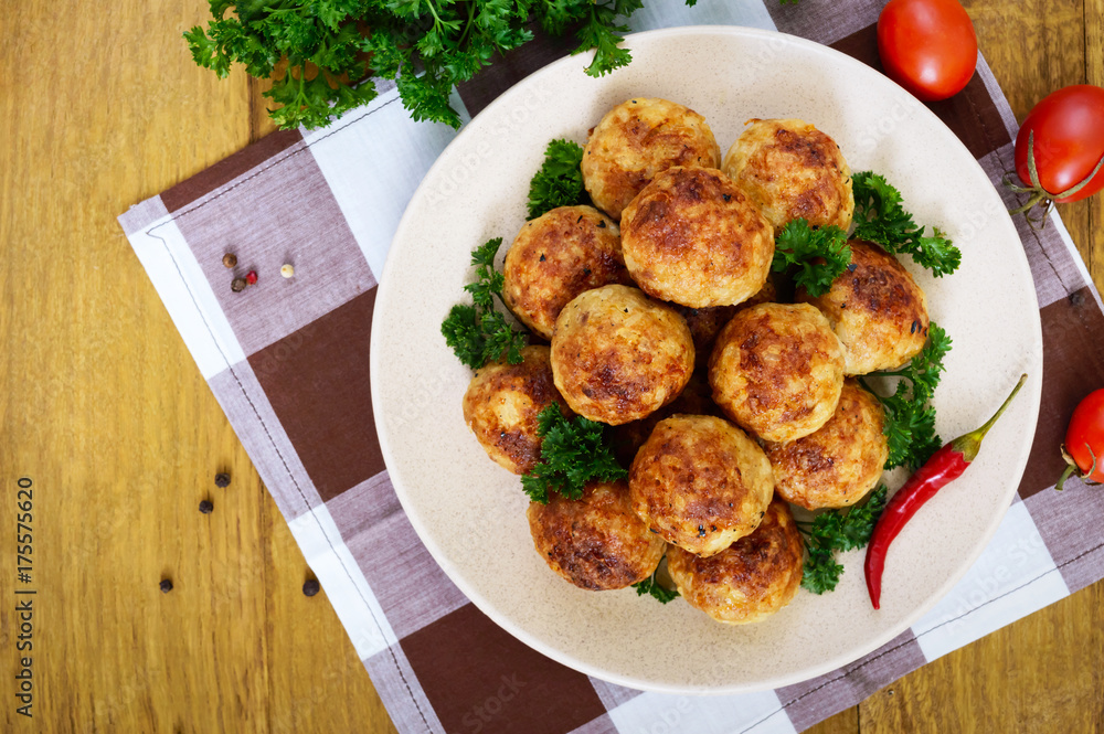 A pile of golden meat balls on a plate with parsley on a wooden table. Top view. A pile of golden meat balls on a plate with parsley on a wooden table. Top view.