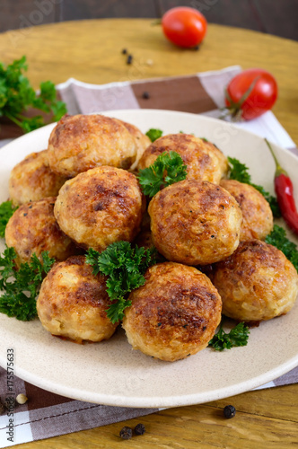 A pile of golden meat balls on a plate with parsley on a wooden table. Close-up. Vertical view