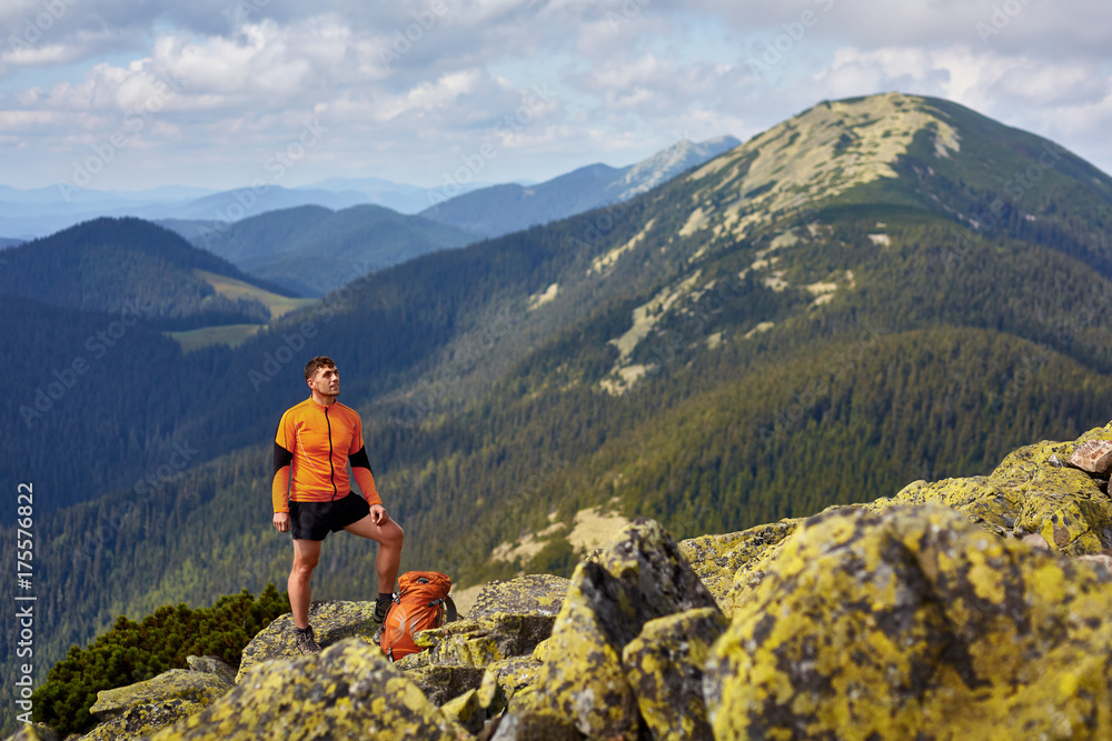 Hiker with backpack standing on top of a mountain with raised hands