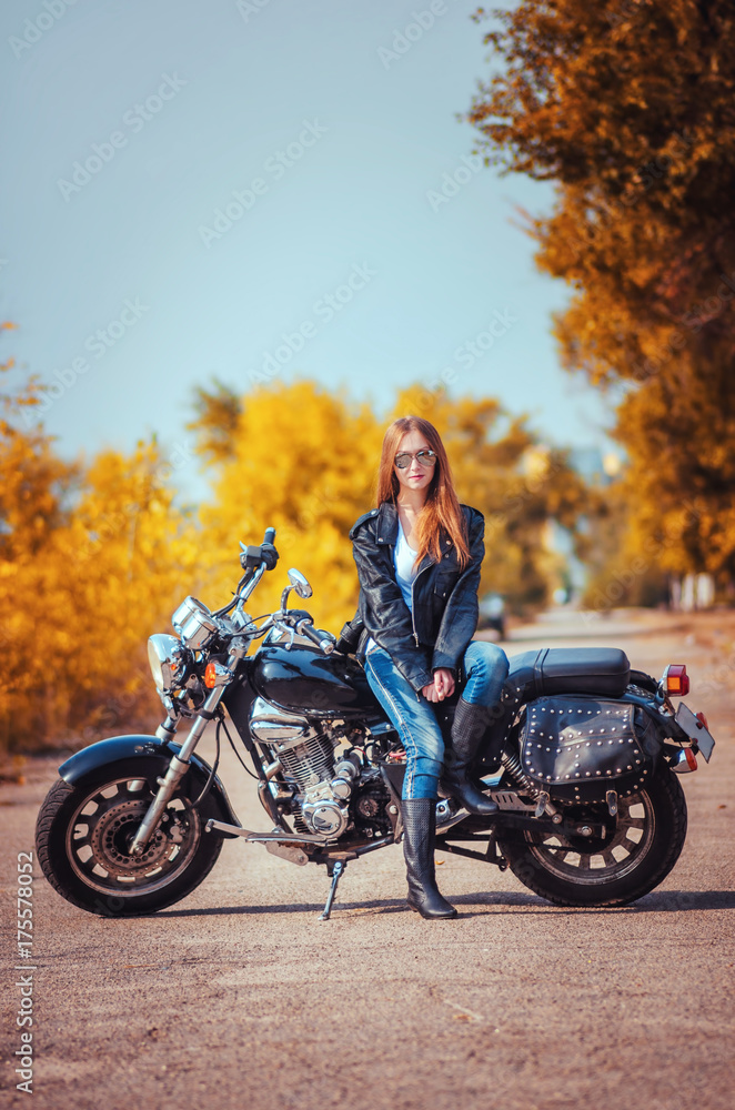 Obraz premium beautiful girl in a leather jacket and blue jeans in a glasses on a motorbike