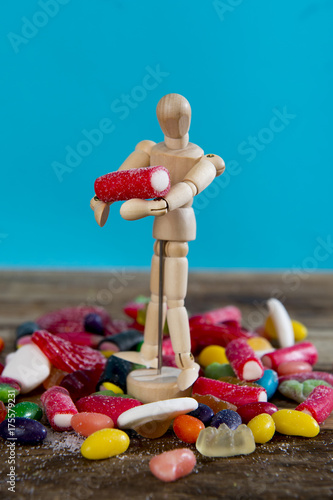 dummy puppet holding and carrying sweet candy upon pile of licorice and caramel gummies