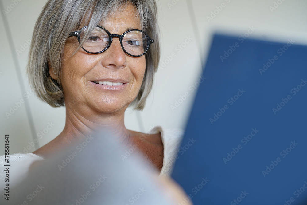 Senior woman with eyeglasses reading book in sofa Senior woman with eyeglasses reading book in sofa