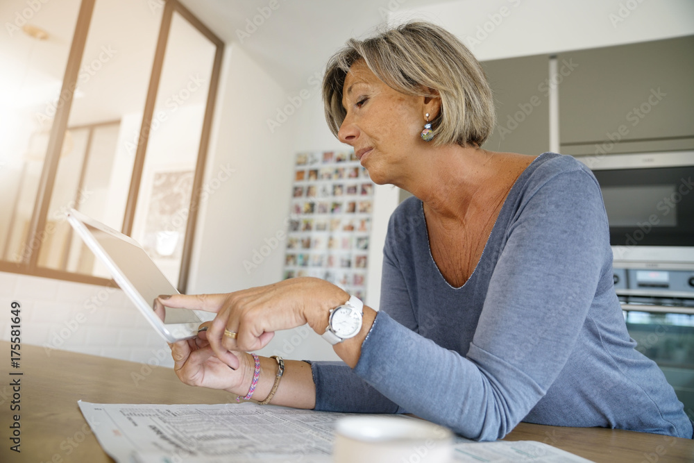 Mature woman at home reading news on digital tablet Mature woman at home reading news on digital tablet