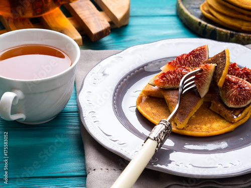 Eating pumpkin pancakes with figs and honey with hot tea. Autumn food background on green wooden table
