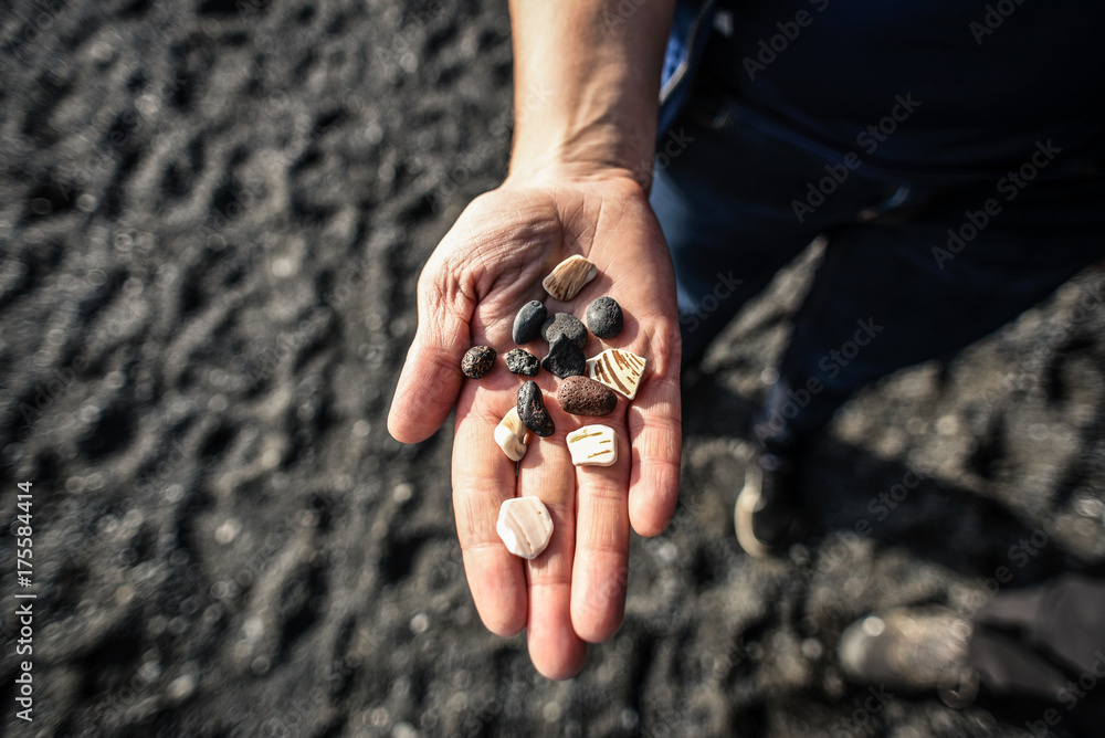 A hand of a woman with stones on it against a background of a black beach in Iceland. A hand of a woman with stones on it against a background of a black beach in Iceland.