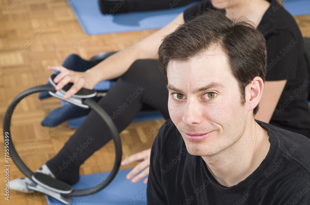 Diverse group of people in a gym class lying in a receding row on mats doing Pilates exercise. Man looking at camera Diverse group of people in a gym class lying in a receding row on mats doing Pilates exercise. Man looking at camera