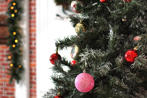 Multicolored Christmas tree toys hang on branches against the decorated door of the house