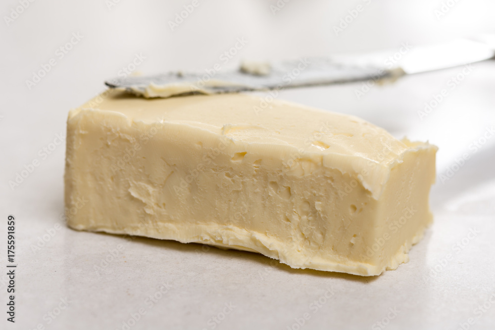 Slice of butter with kitchen knife on the white marble background table