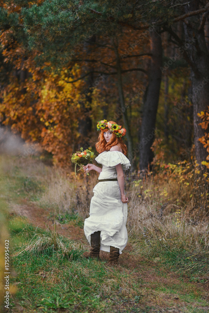 Fototapeta premium Autumn romantic red-haired woman runs along a forest road