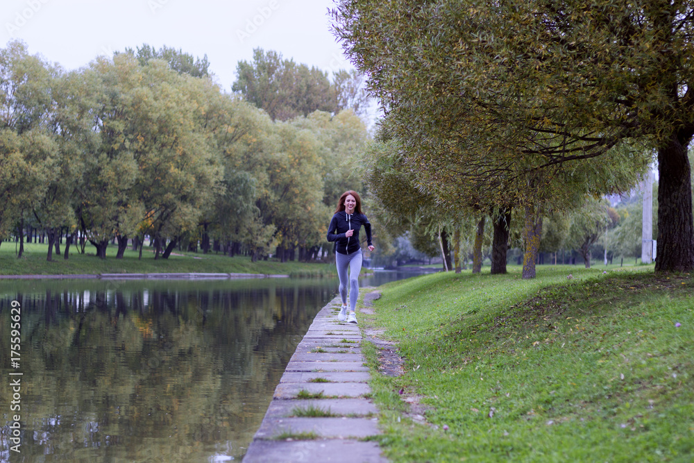Young happy woman jogging in autumn nature on the bank of river. Running Fitness girl