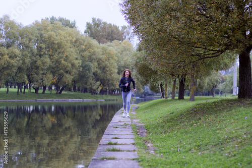 Young happy woman jogging in autumn nature on the bank of river. Running Fitness girl