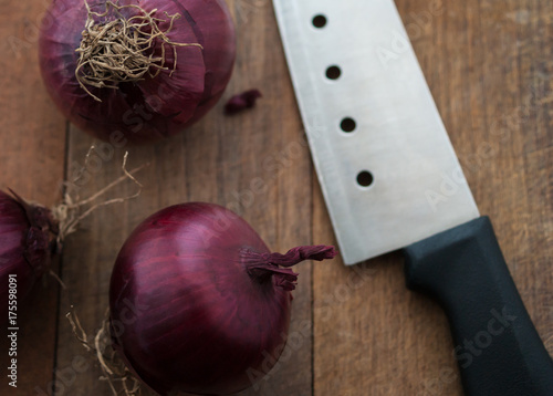 Food preparation, cooking concept: fresh raw red onions, knife on a rustic wooden cutting board background photo