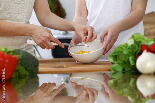 Close-up of human hands cooking in a kitchen. Friends having fun while preparing fresh salad. Vegetarian, healthy meal and friendship concept