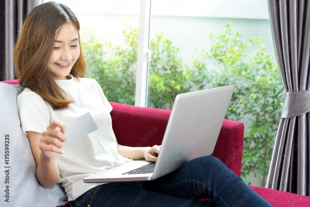Young asian woman holding card with laptop computer for online shopping payment on sofa relaxing at home Young asian woman holding card with laptop computer for online shopping payment on sofa relaxing at home