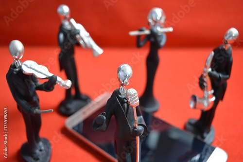 Toy man with microphone and musicians around a mobile phone on red background.