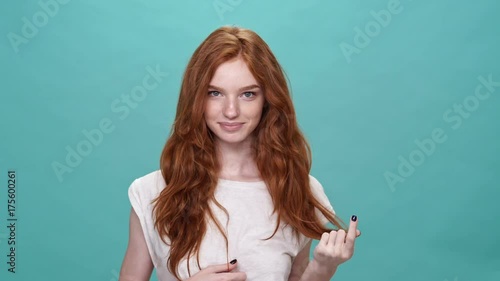 Smiling ginger woman in t-shirt posing and looking at the camera over turquoise background