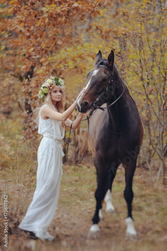 autumn portrait of romantic woman with flowers in her hair near with a horse