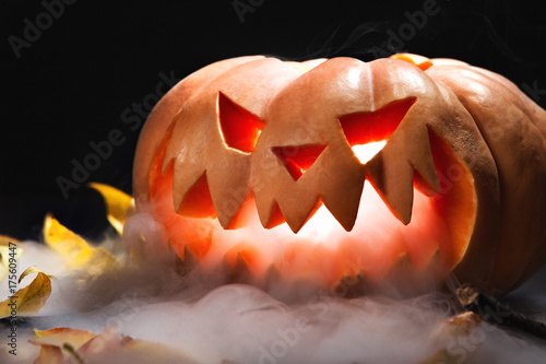 Halloween pumpkin lantern with dry leaves with burning candles