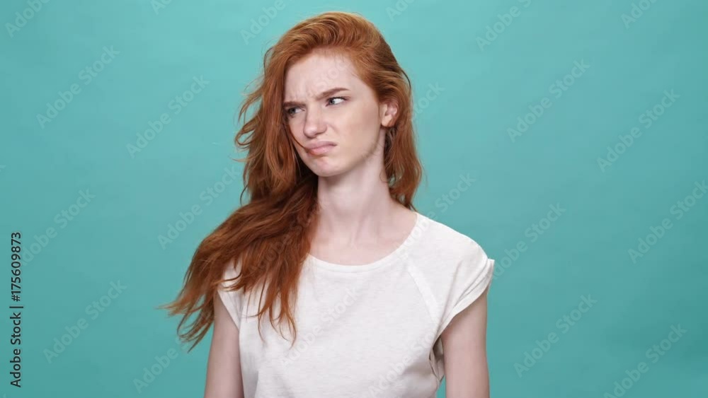 Upset ginger woman in t-shirt wants to cut off her hair over turquoise background Upset ginger woman in t-shirt wants to cut off her hair over turquoise background
