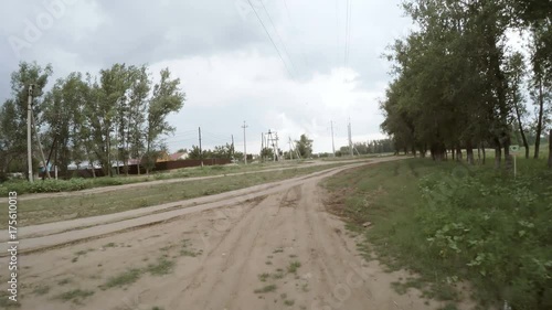 A view of the rural dirt road from camera installed on back of the car driving along this country road. Riding on a rough roadway. High voltage power line pylon. Traces of tires on the sand.