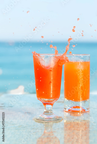Two glasses with a cocktail of orange juice against the blue sea.