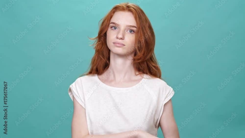 Pretty ginger woman corrects her t-shirt and looking at the camera over turquoise background Pretty ginger woman corrects her t-shirt and looking at the camera over turquoise background