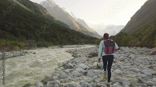 Young woman walking along the river by the mountain creek, facing away from the camera.