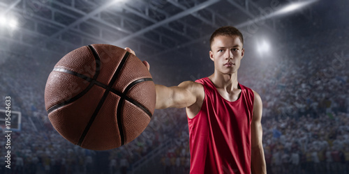 Basketball player hold a basketball ball on big professional arena. Player wears unbranded clothes.